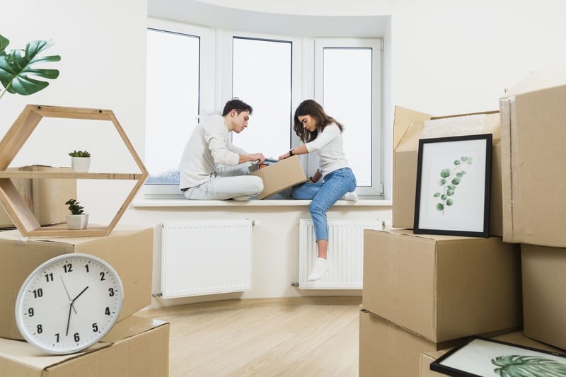 young couple sitting window sill unpacking cardboard boxes